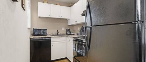 A compact kitchen with white cabinets, a black refrigerator, a microwave, a coffee maker, and a dishwasher.
