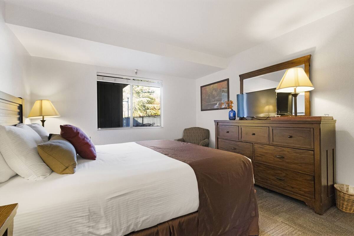 A bedroom with a bed, a dresser, a chair, a window, and a lamp.