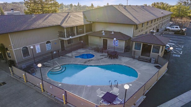 A hotel with a swimming pool, outdoor seating, and a parking lot.