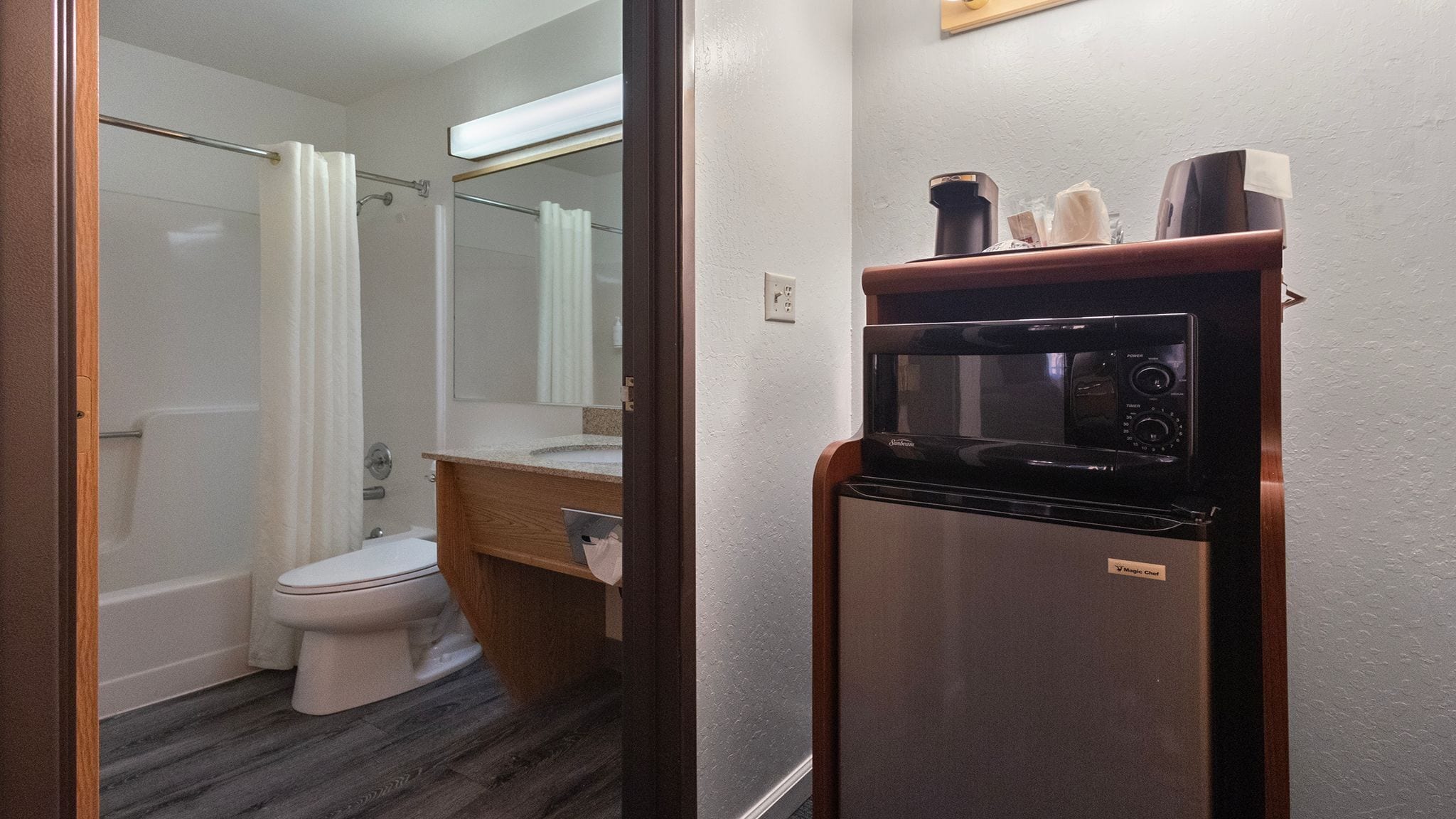 A compact bathroom with a toilet, sink, and shower. A microwave is placed on a wooden cabinet.