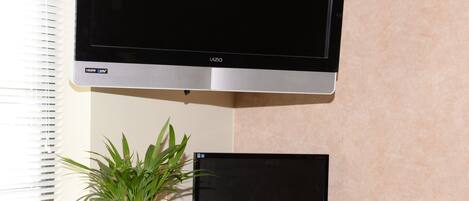 A workspace with a flat-screen TV, a smaller monitor, a keyboard, a mouse, a chair, and a potted plant.