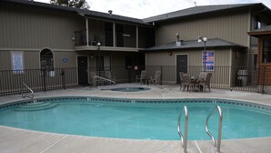 A swimming pool with a hot tub, surrounded by a fence and chairs.