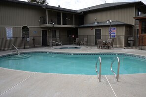 A swimming pool with a hot tub, surrounded by a fence and chairs.
