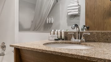 A bathroom with a granite countertop, two sinks, a mirror, and a towel rack.