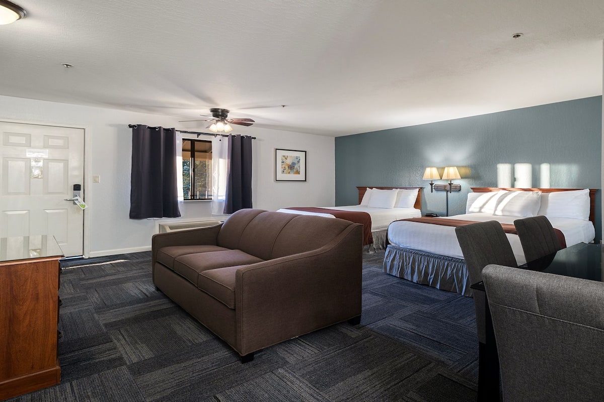 A hotel room with two beds, a sofa, a desk, and a ceiling fan.