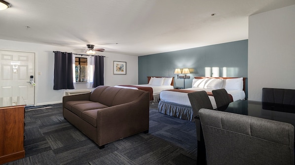 A hotel room with two beds, a sofa, a desk, and a ceiling fan. - Aladdin Inn (Sonora)