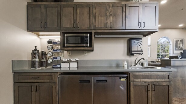 Una cucina con mobili impiallacciati in legno scuro, lavastoviglie in acciaio inox, microonde e macchina da caffè.