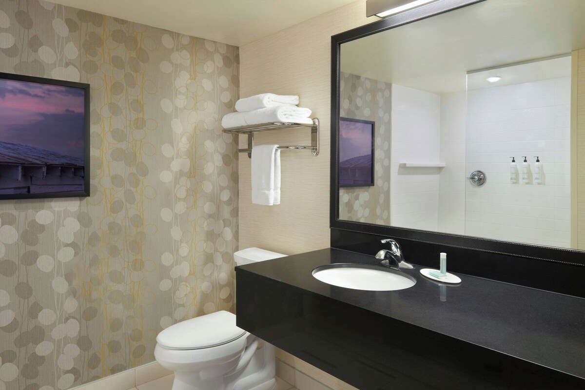 Un baño moderno con lavamanos negro, inodoro blanco y un espejo grande.
