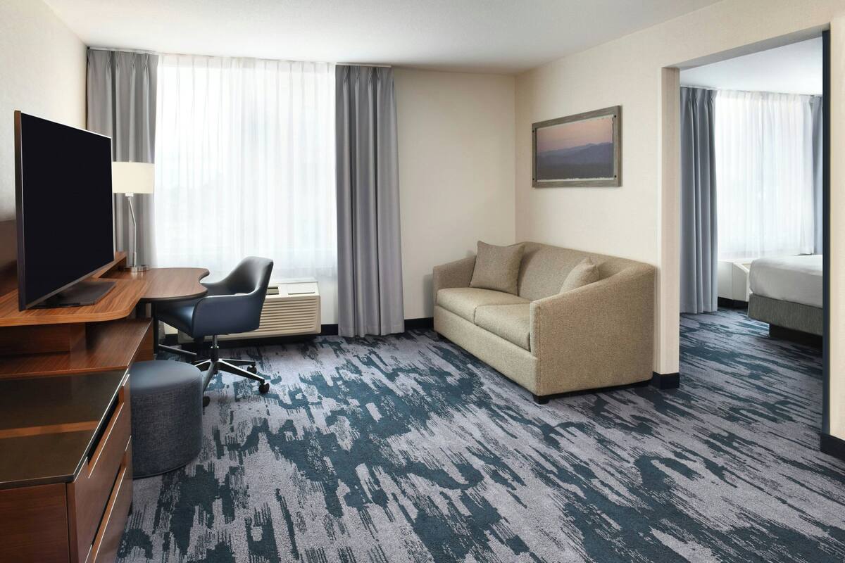 A hotel room with a desk, chair, sofa, and a TV.