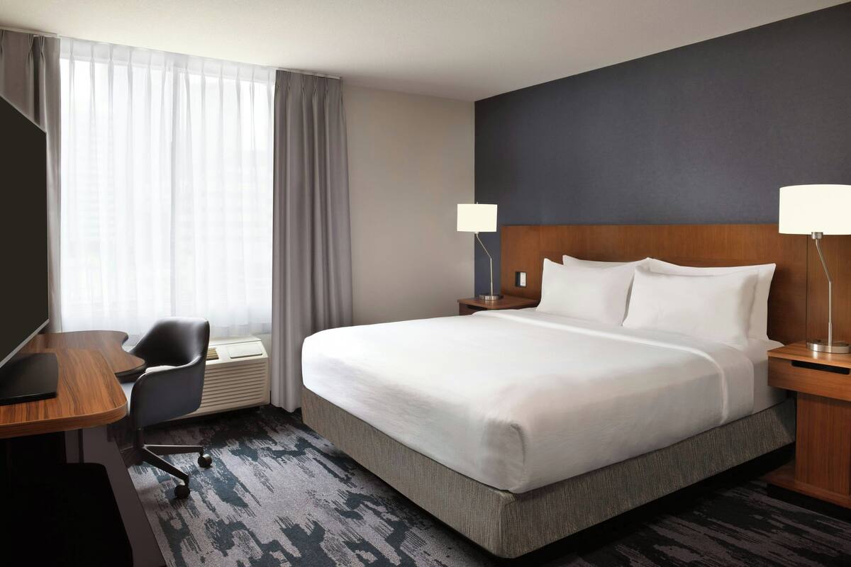 A hotel room with a large bed, a desk, a chair, a lamp, and a window with curtains.