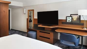 Habitación de hotel con cama, escritorio, televisor de pantalla plana, silla, lámpara de escritorio y espejo.