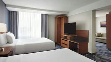 A hotel room with two beds, a TV, a desk, and a sofa.