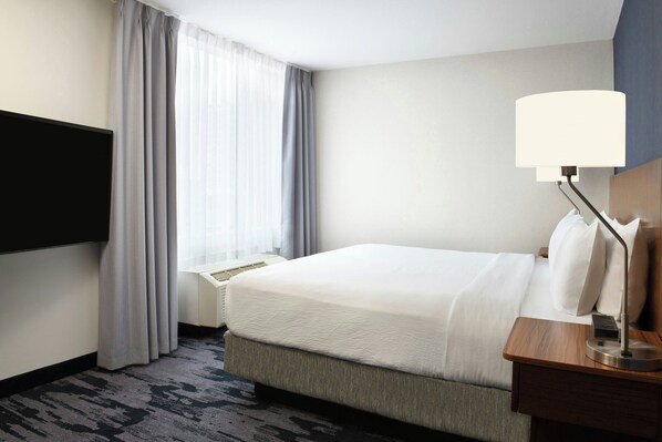 Habitación de hotel con cama, mesita de noche con lámpara, televisor de pantalla plana en la pared y ventana con cortinas.