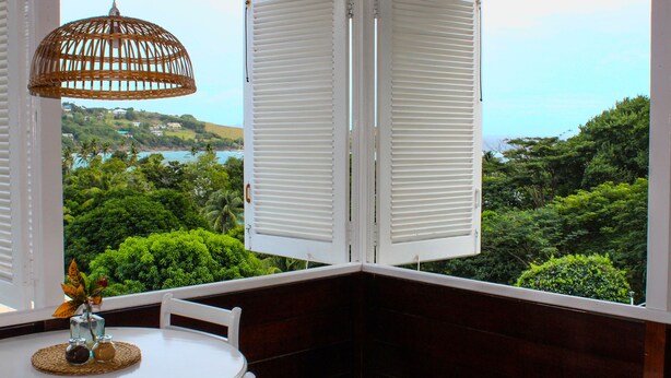 A corner room with a view of lush greenery and a body of water. - Sugarapple Inn (Bequia Island)