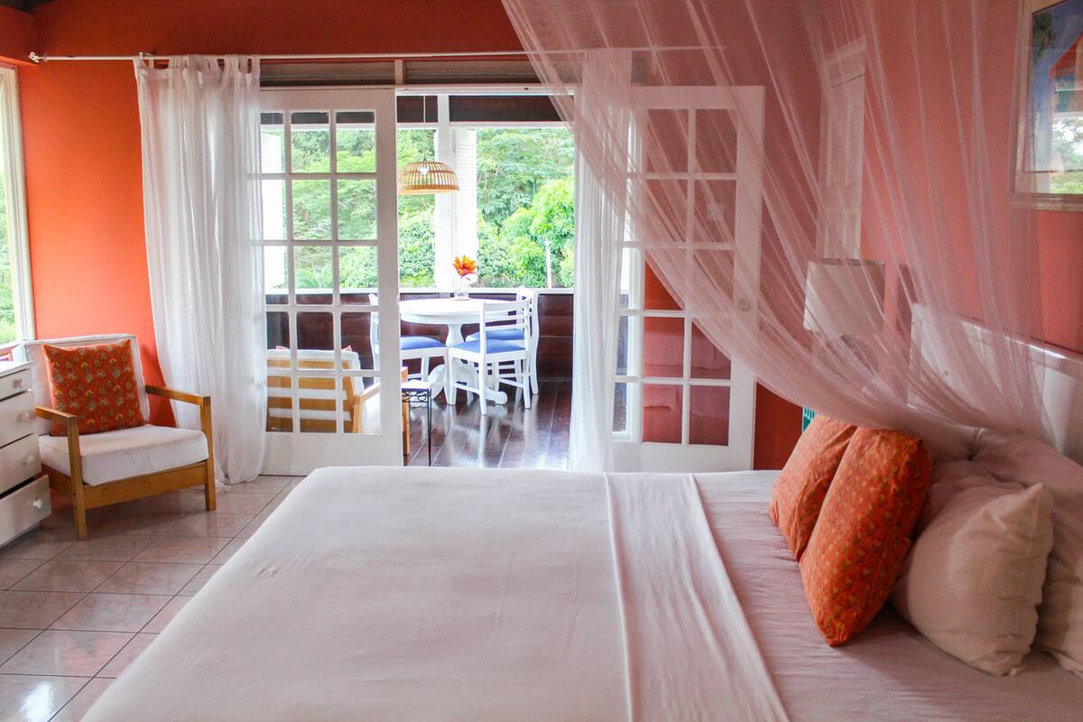 A bedroom with a large bed, a chair, a table, and a view of the outdoors through a sliding door.