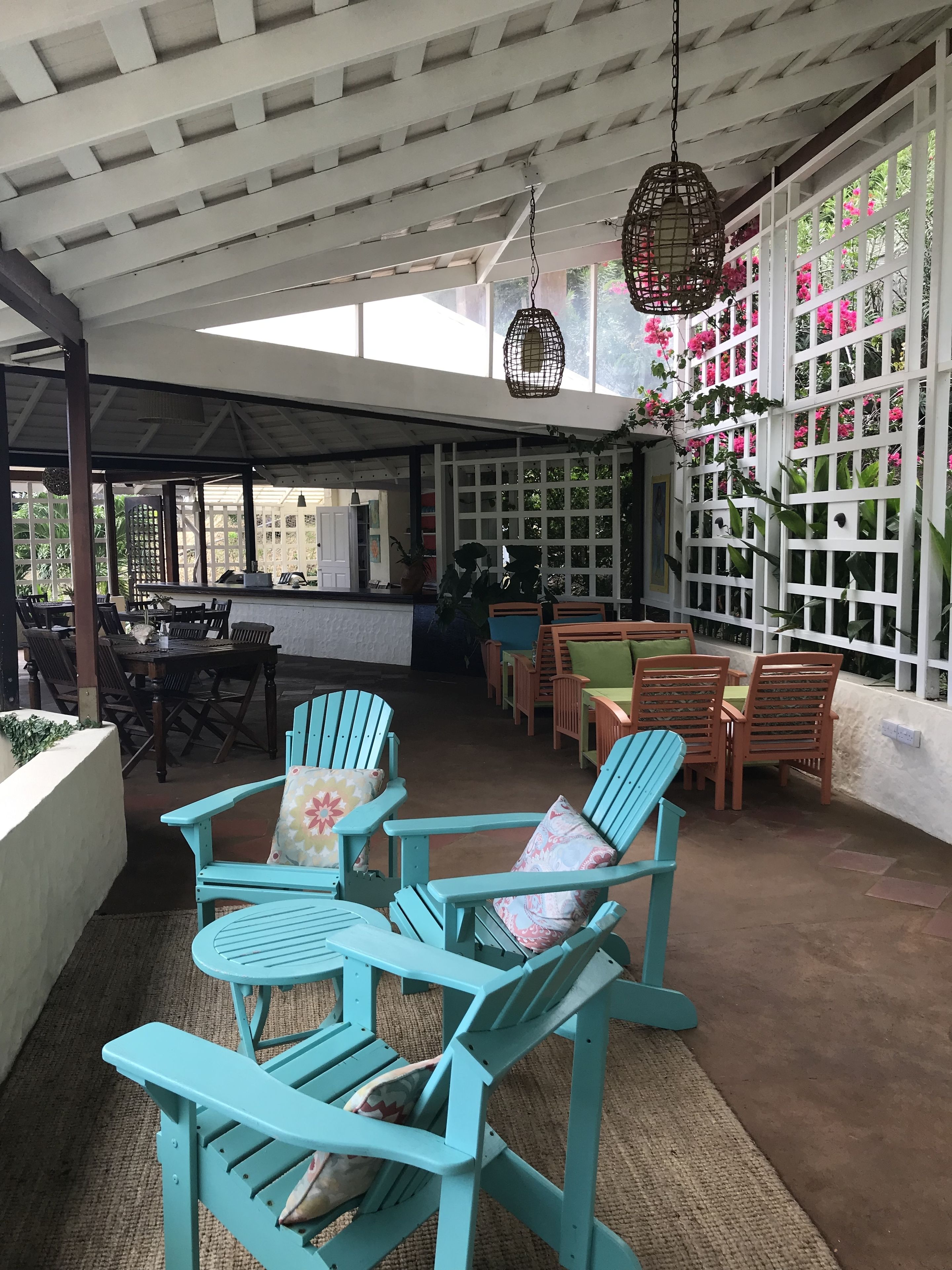 Een overdekt terras met turquoise Adirondack-stoelen en een eettafel.