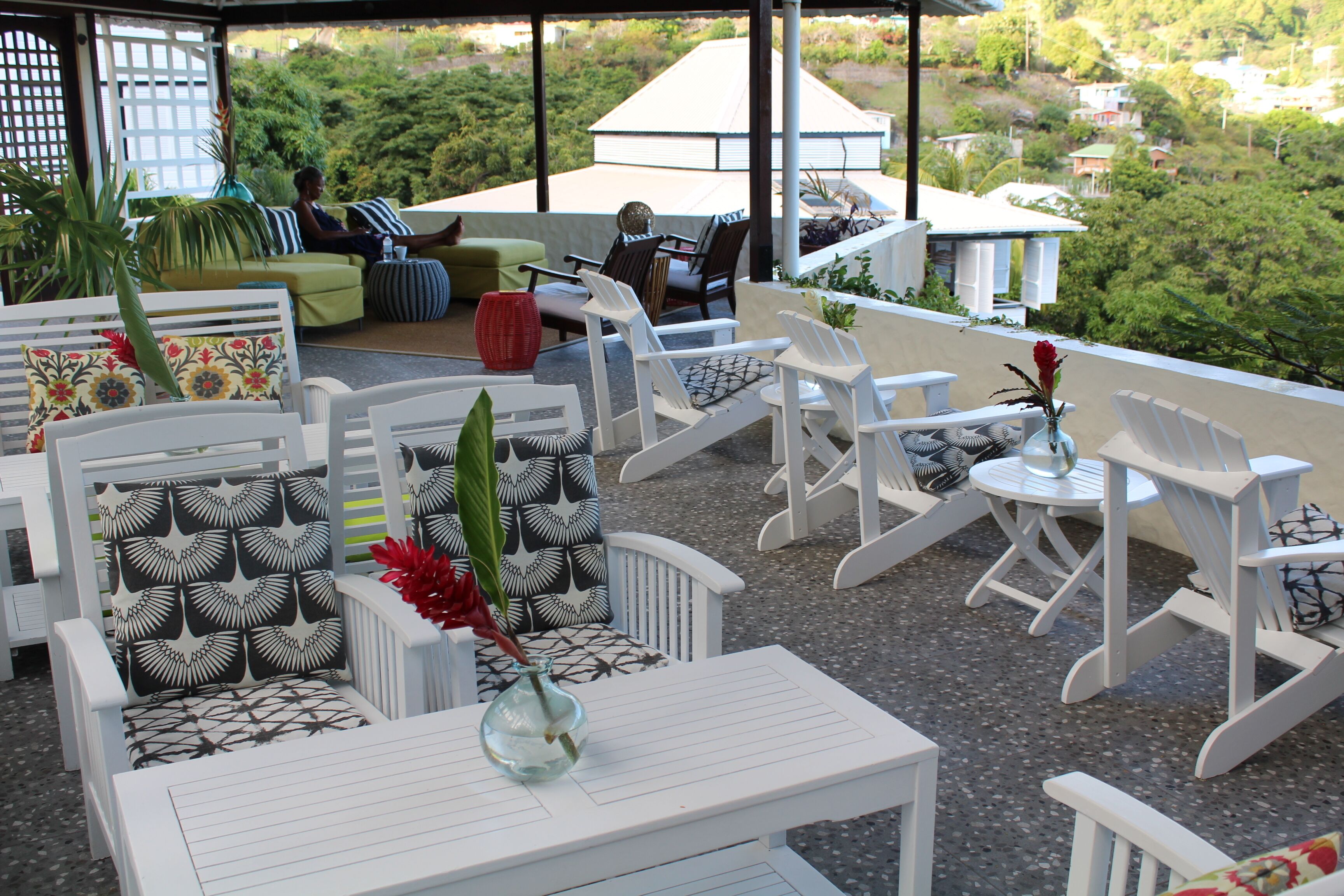 A terrace with white furniture, including chairs and a table, and a view of the surrounding greenery and buildings.