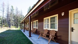 A cabin with a porch, wooden chairs, and a door. - Rising Sun Motor Inn and Cabins - Inside the Park (East Glacier Park)