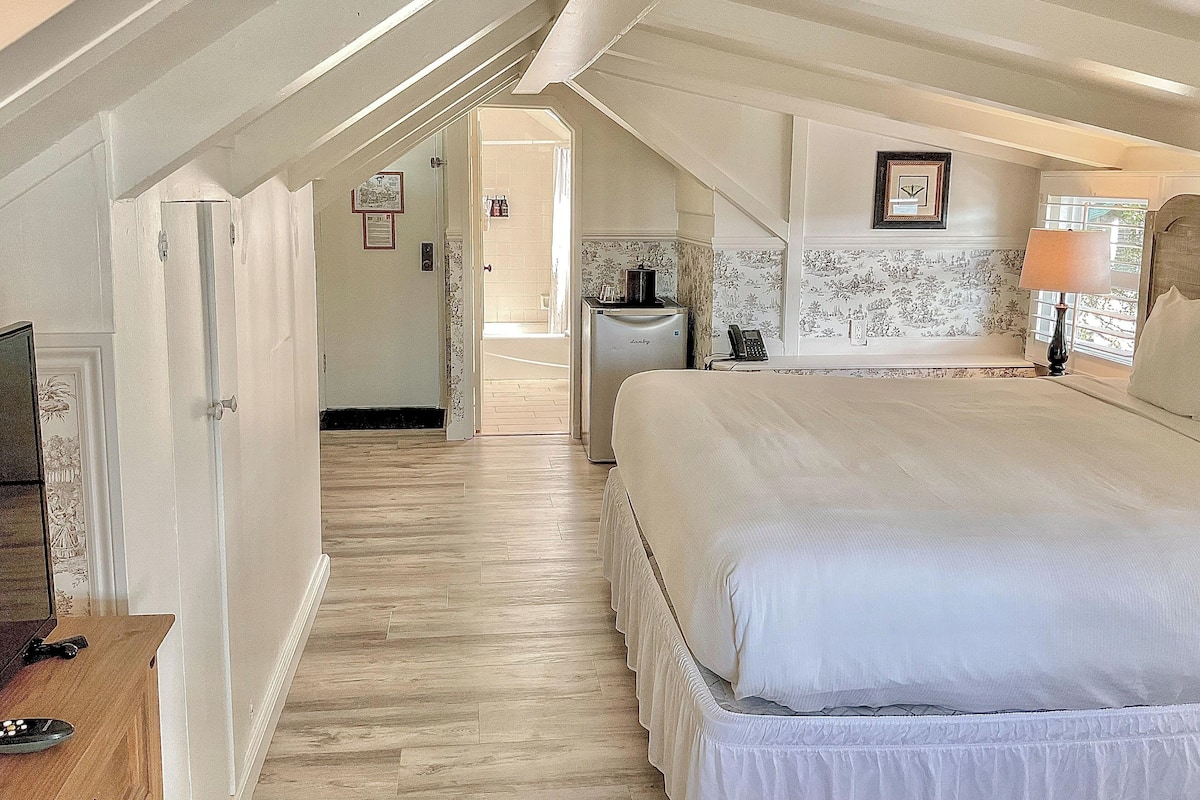 A bedroom with a large bed, a bedside table, a lamp, and a view of the bathroom.