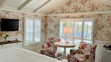 A bedroom with a bed, a TV mounted on the wall, a table with chairs, and a window with blinds.