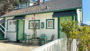 A house with a green door, a small porch with green chairs, and a white fence.
