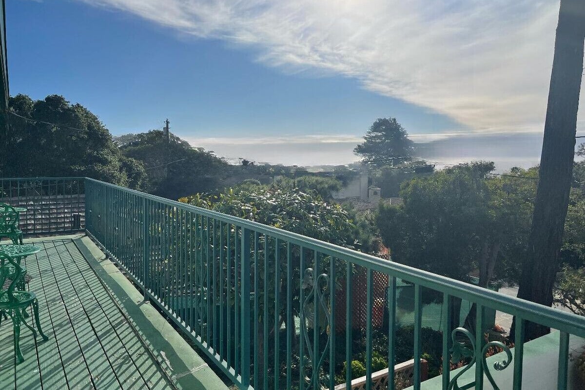 A balcony with a green railing overlooking a lush landscape with trees and a distant view of a body of water.