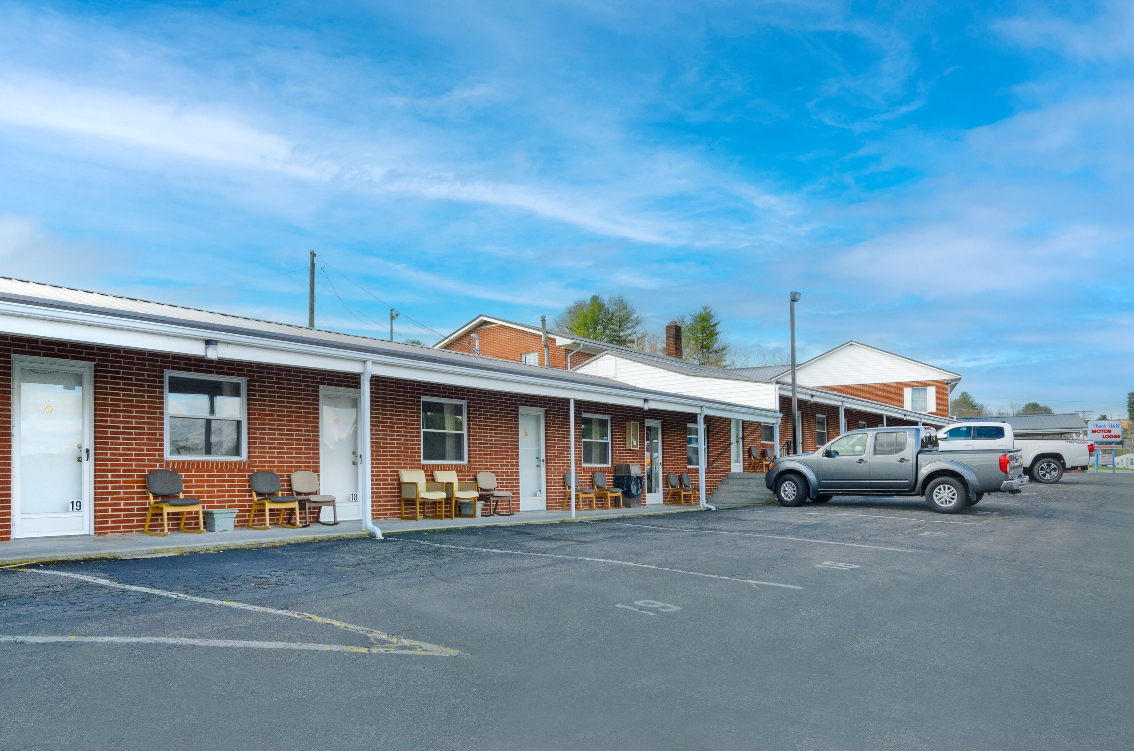 Motel amb una filera d'habitacions, zones d'estar a l'exterior i un pàrquing.