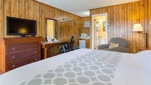 Ein Hotelzimmer mit Holzvertäfelung, einem Bett mit gebogener Tagesdecke, einem Schreibtisch mit Computer, einem Fernseher und einem Sessel.
