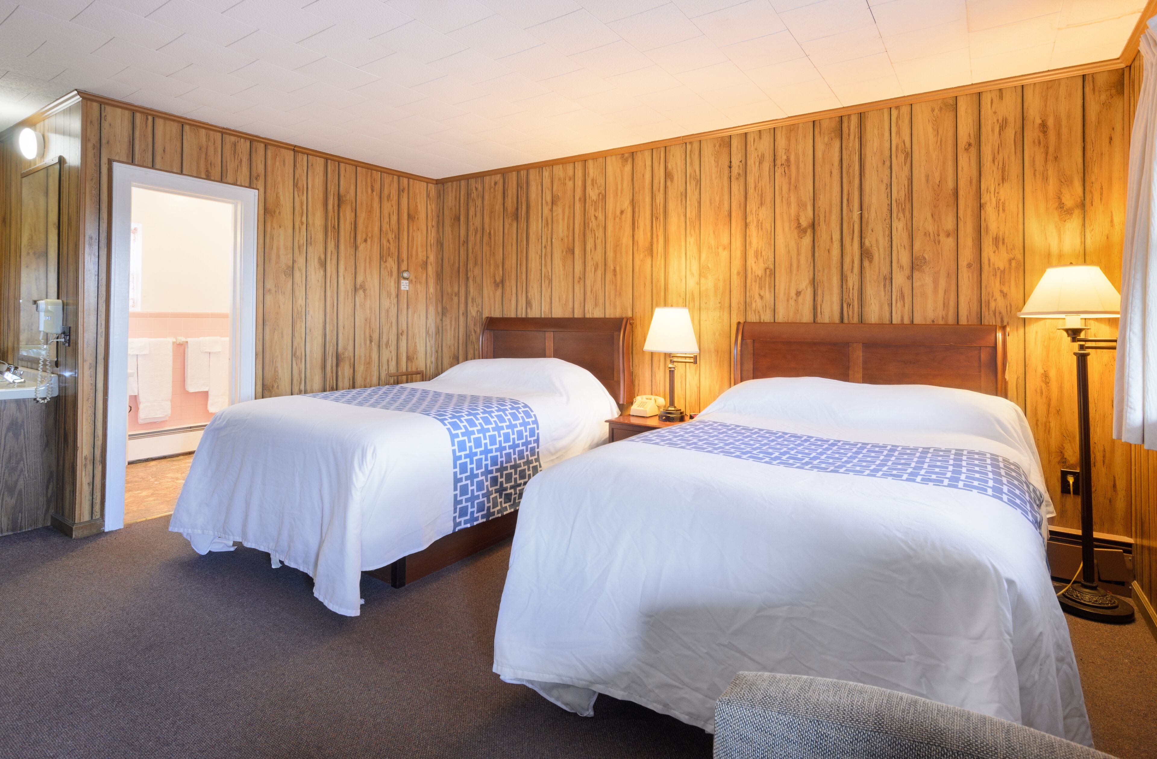 A hotel room with two beds, wooden paneling on the walls, and a door leading to a balcony.