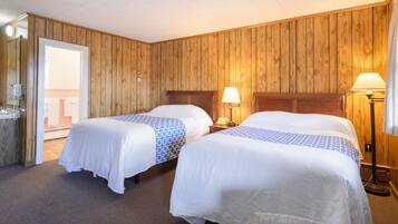 A hotel room with two beds, wooden paneling on the walls, and a door leading to a balcony.