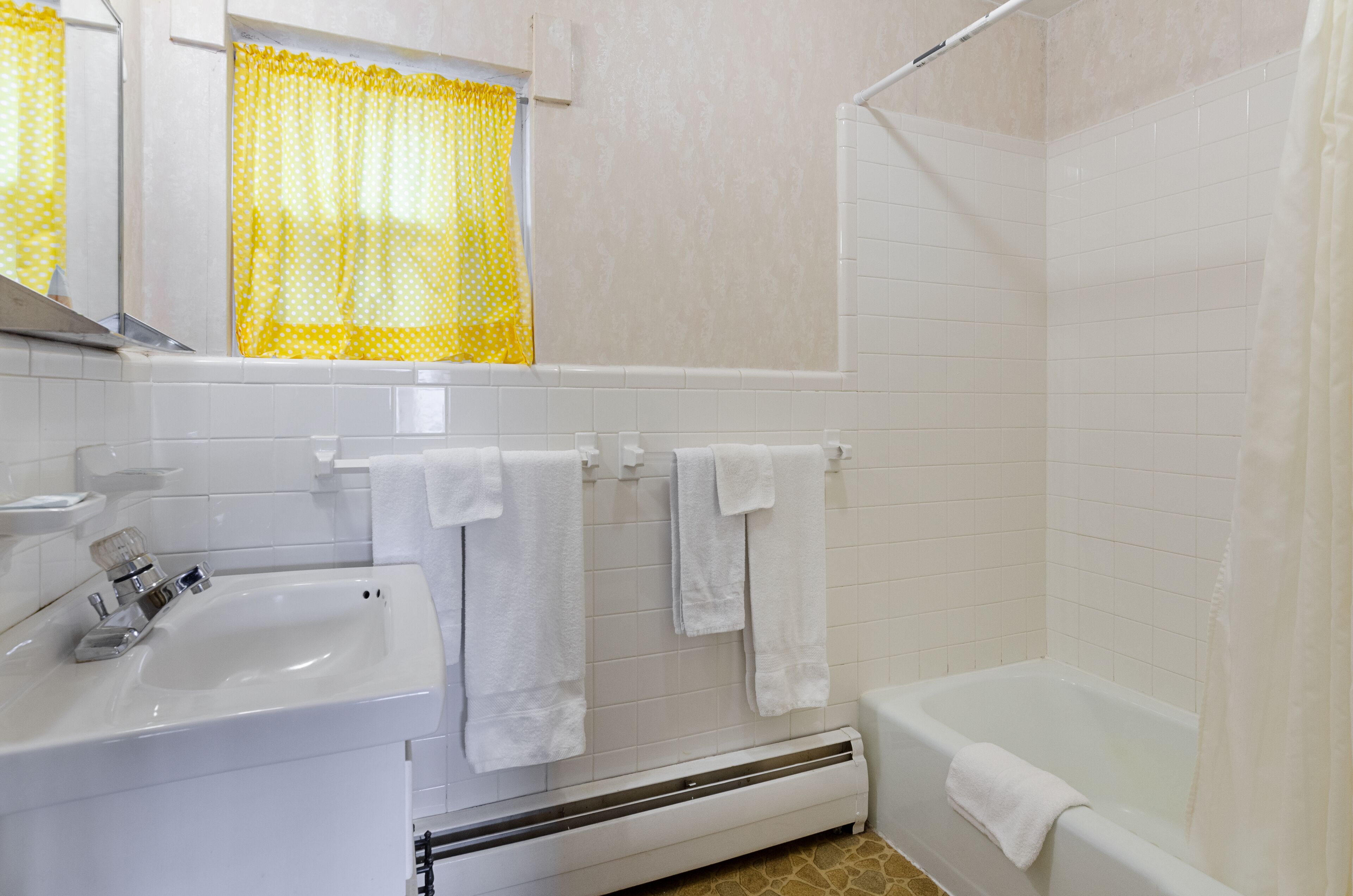 Un baño con lavamanos, espejo, toallero y bañera.