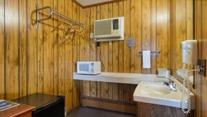 Ein kleines Badezimmer mit Holzwänden, einem Waschbecken, einem Spiegel, einer Mikrowelle und einem Föhn.