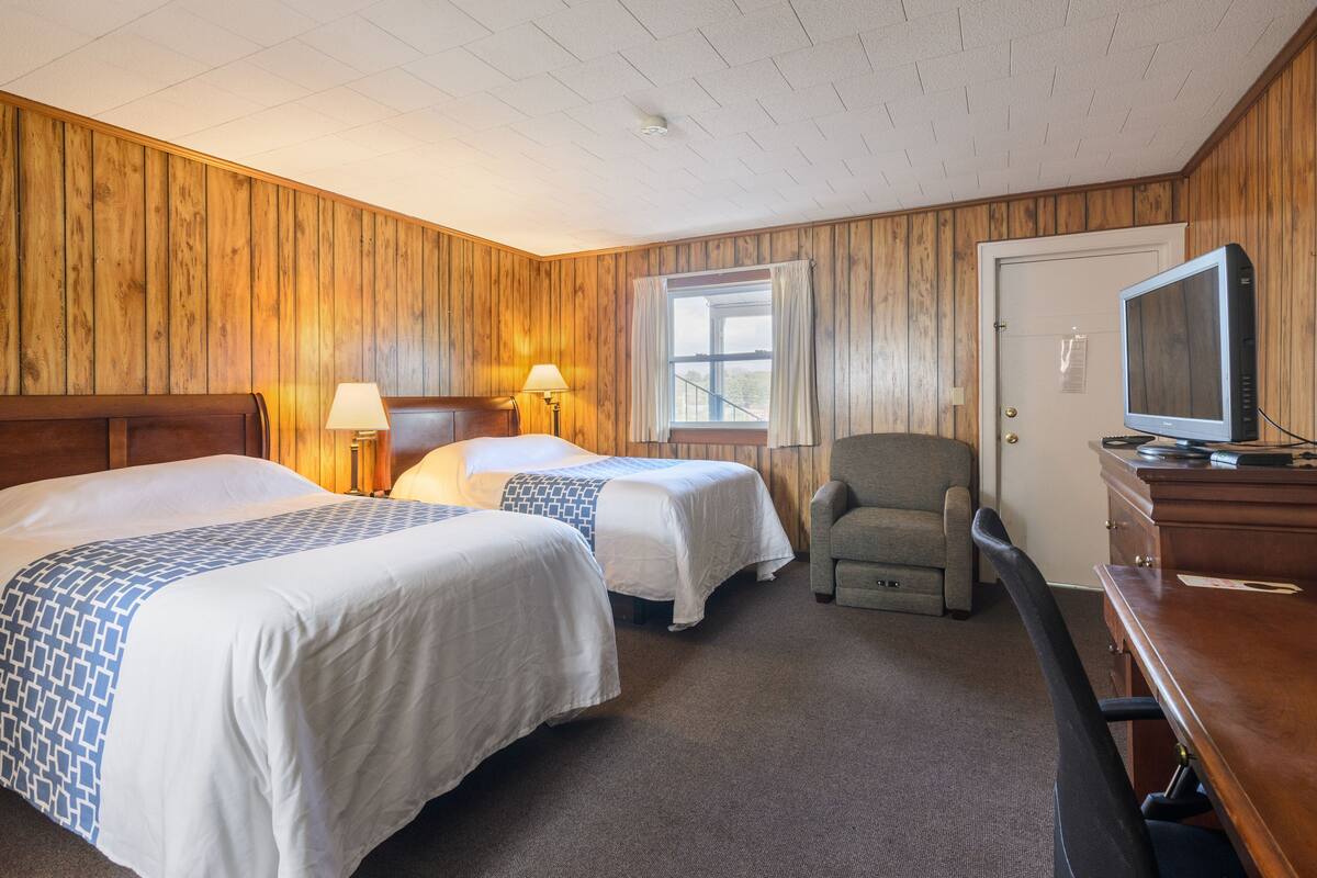 Une chambre d’hôtel avec deux lits, un bureau, une chaise, une télévision et une fenêtre avec des rideaux.