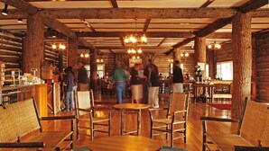 A rustic wooden interior with high ceilings, exposed beams, and a central chandelier. Tables and wicker chairs are arranged for dining. - Roosevelt Lodge & Cabins - Inside the Park (Yellowstone National Park)