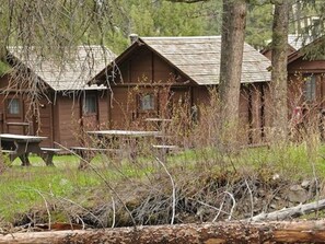 A rustic cabin with a wooden exterior, a small porch, and a picnic table in front. - Roosevelt Lodge & Cabins - Inside the Park (Yellowstone National Park)