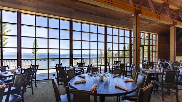 Un restaurante con amplios ventanales que ofrecen vista al mar. Las mesas están dispuestas con cubiertos y copas.