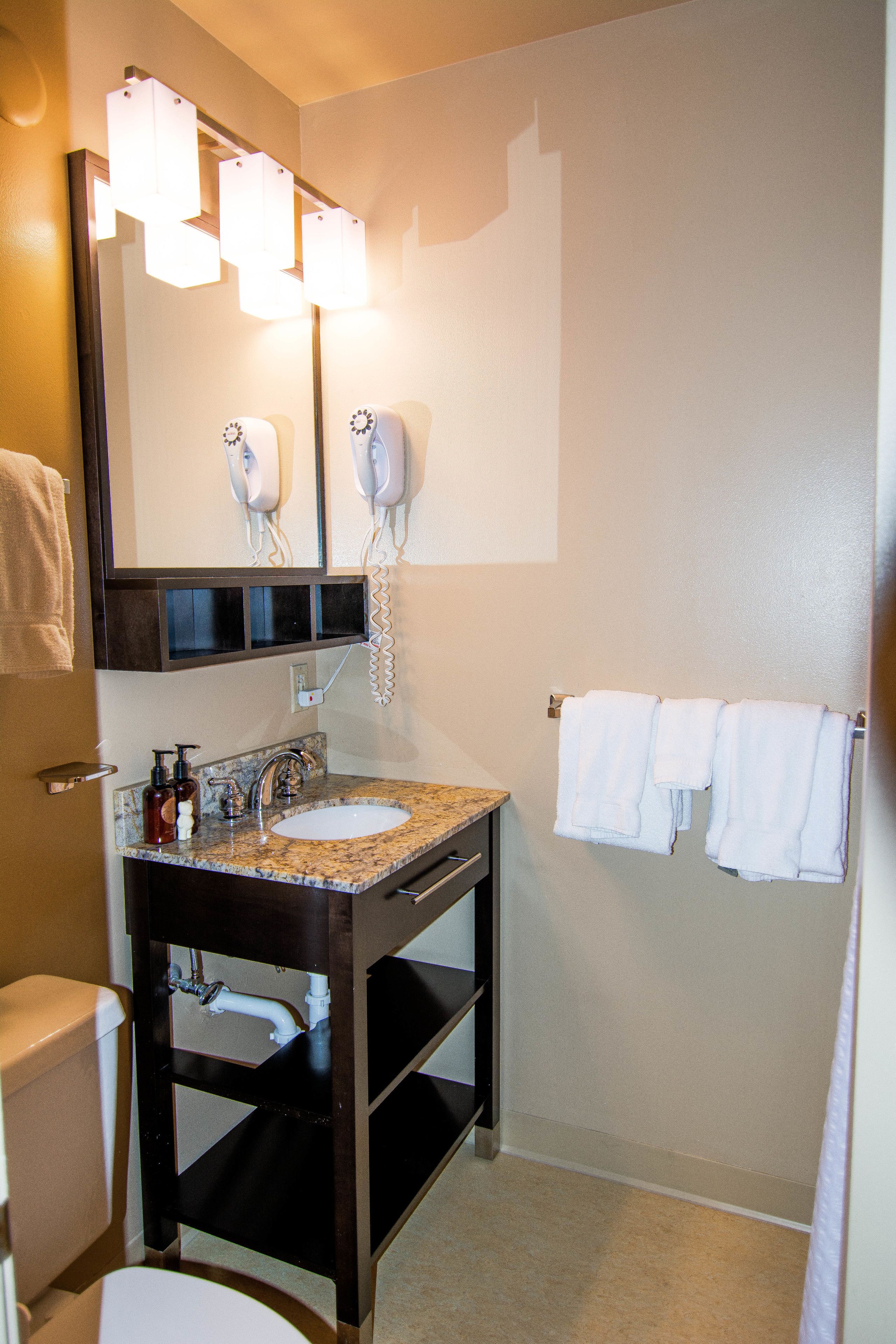 A bathroom with a sink, mirror, hairdryer, and two towels hanging on the wall.