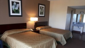 Habitación de hotel con dos camas, una mesita de noche con lámpara y cuadros en las paredes.