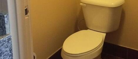 A small bathroom with a toilet, a towel rack with two towels, and a door leading to another room.