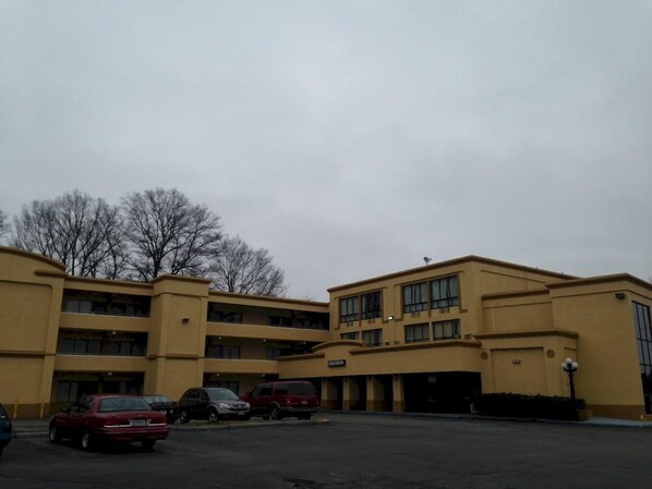 A multi-story hotel with a yellow facade, multiple parking spaces, and a flat roof.
