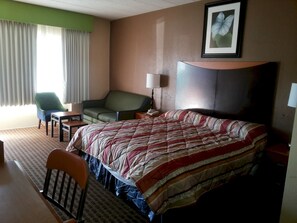 A hotel room with a large bed, a desk, a chair, a sofa, and a framed picture on the wall.