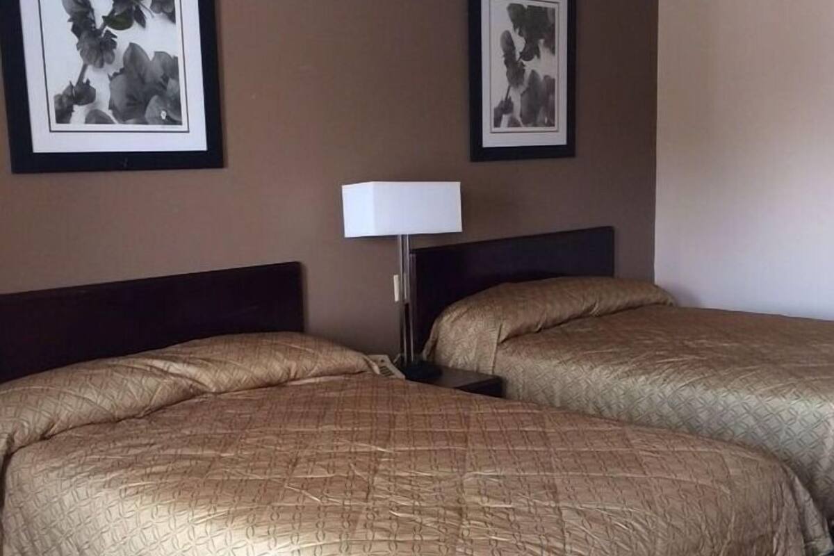 A hotel room with two beds, a nightstand, a lamp, and two framed pictures on the wall.