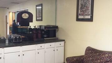 A small, enclosed room with a kitchenette area, a patterned armchair, and a round table.