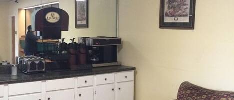 A small, enclosed room with a kitchenette area, a patterned armchair, and a round table.