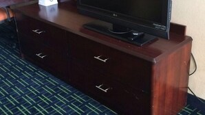 Habitación de hotel con televisión de pantalla plana sobre una cómoda de madera, una caja de pañuelos y un espejo en la pared.
