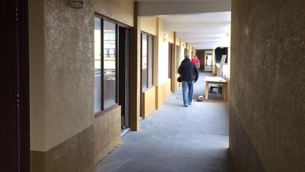 Un pasillo con piso de concreto y paredes color beige, que conduce a una habitación con cama y ventana.