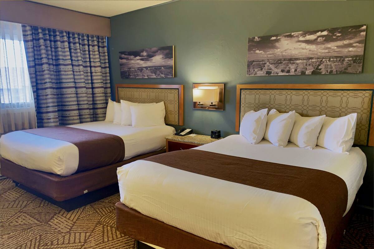 Habitación de hotel con dos camas, alfombra estampada y dos lámparas fijadas a la pared.