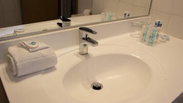 Un bagno d'hotel con un lavandino bianco, uno specchio e articoli da toilette sul ripiano.