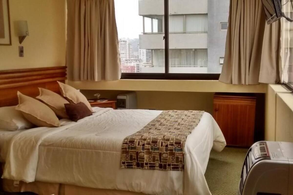 Ein Hotelzimmer mit Bett, einem Fenster mit Vorhängen, einem Heizkörper und einem Wandheizgerät.