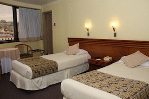 Ett hotellrum med två sängar, ett litet bord, en stol och ett fönster med utsikt över stadsbilden.